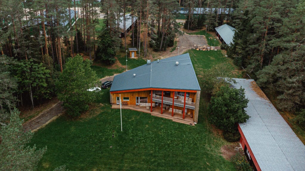 Droonivaade kaasaegsest puidust hoonest metsaserval, mille ümbrust ümbritseb rohelus ja kõrval paiknevad abiehitised.