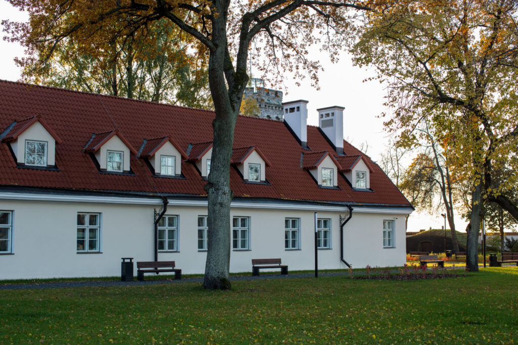 Maarjamäe kompleksi renoveeritud kõrvalhoone – valge fassaad ja punane viilkatus katuseakendega, ümberringi sügisvärvides puud ja hooldatud park pingiridadega.