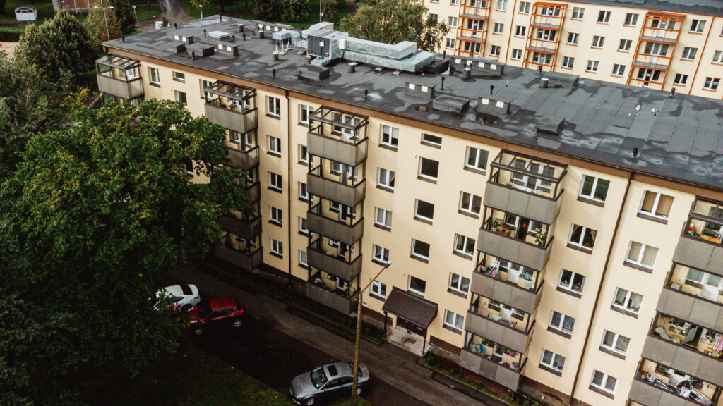 Õhust vaade renoveeritud korterelamule, millel on soojustatud fassaad ja klaasitud rõdud. Maja ees parkivad autod ja kõrvale jääb haljasala.