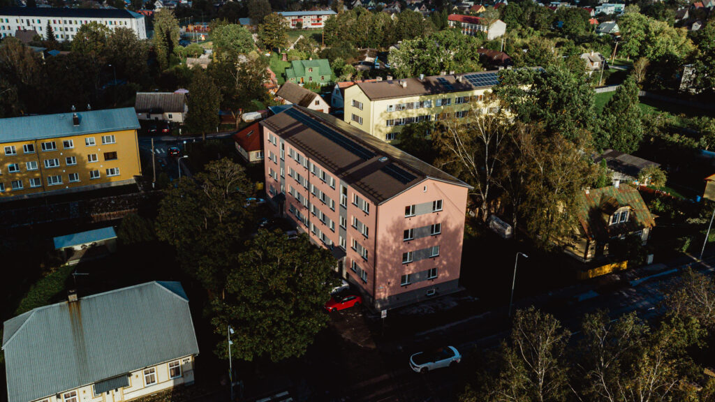 Õhust vaade renoveeritud roosale korterelamule, mille ümber paiknevad elumajad ja haljastatud aedadega hoovid sügiseses valguses.