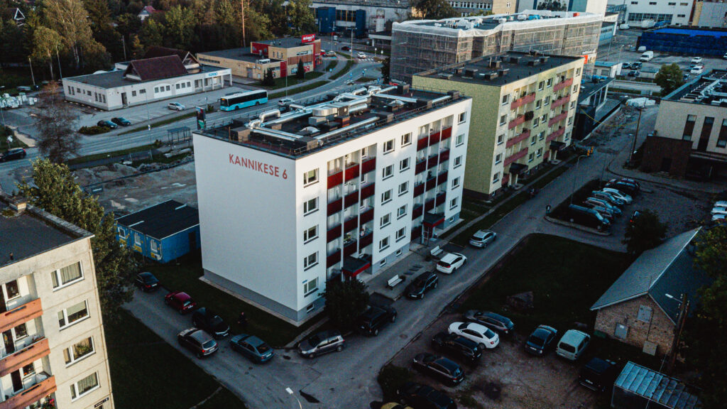 Droonifoto korterelamust Kannikese 6, millel on valge fassaad ja punased rõdud; ümbruses teised majad, parkivad autod ja taustal linnatänav koos bussipeatusega.