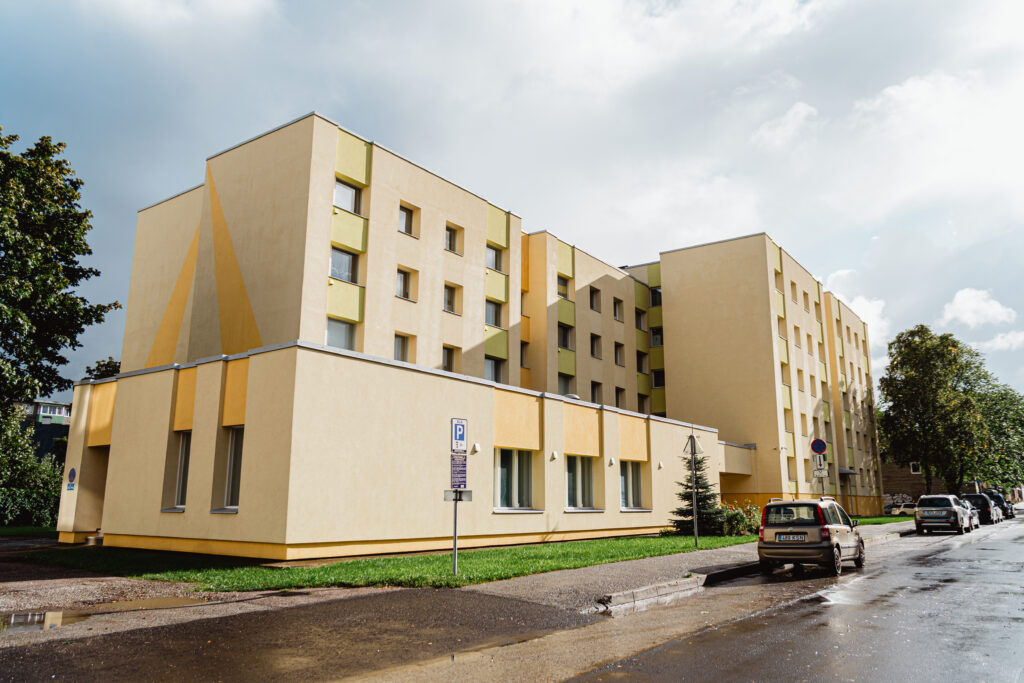 Katusepapi 23 korterelamu tänavavaade, millel on heledates toonides renoveeritud fassaad roheliste ja kollaste aktsentidega ning märg asfalt vihma järel.